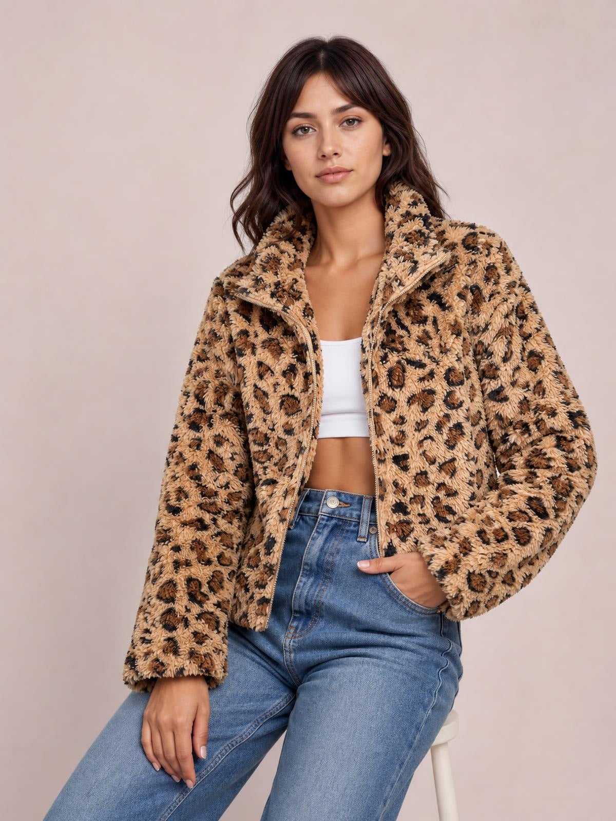 Model seated in a fuzzy tan-and-black leopard zip-up jacket with a high turtleneck collar, long sleeves, relaxed silhouette, and one hand in a pocket.