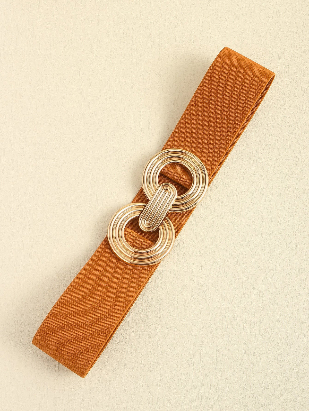 Rust-orange elastic wide belt with a broad, clean band and a dimensional alloy geometric buckle featuring interlocking rounded forms.