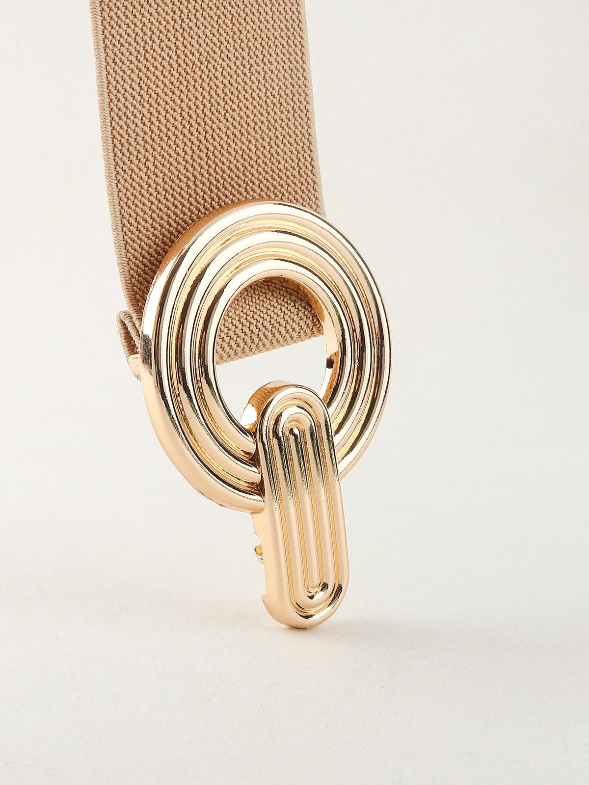 Close-up of a tan elastic wide belt featuring a polished gold alloy geometric buckle with layered rounded forms and a textured woven band.