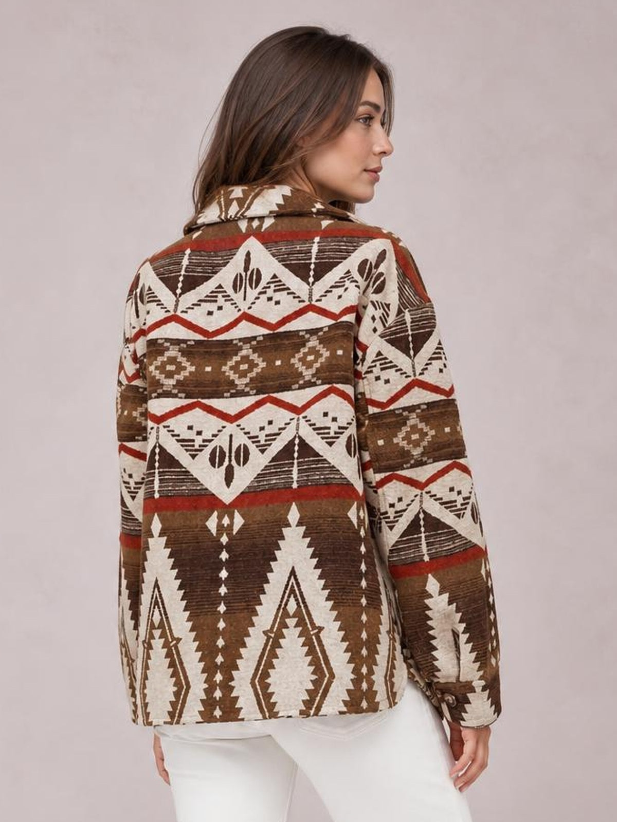 A woman turns in profile to show a relaxed geometric button-up jacket with long sleeves, a collar, and bold brown, cream, and red patterned bands.