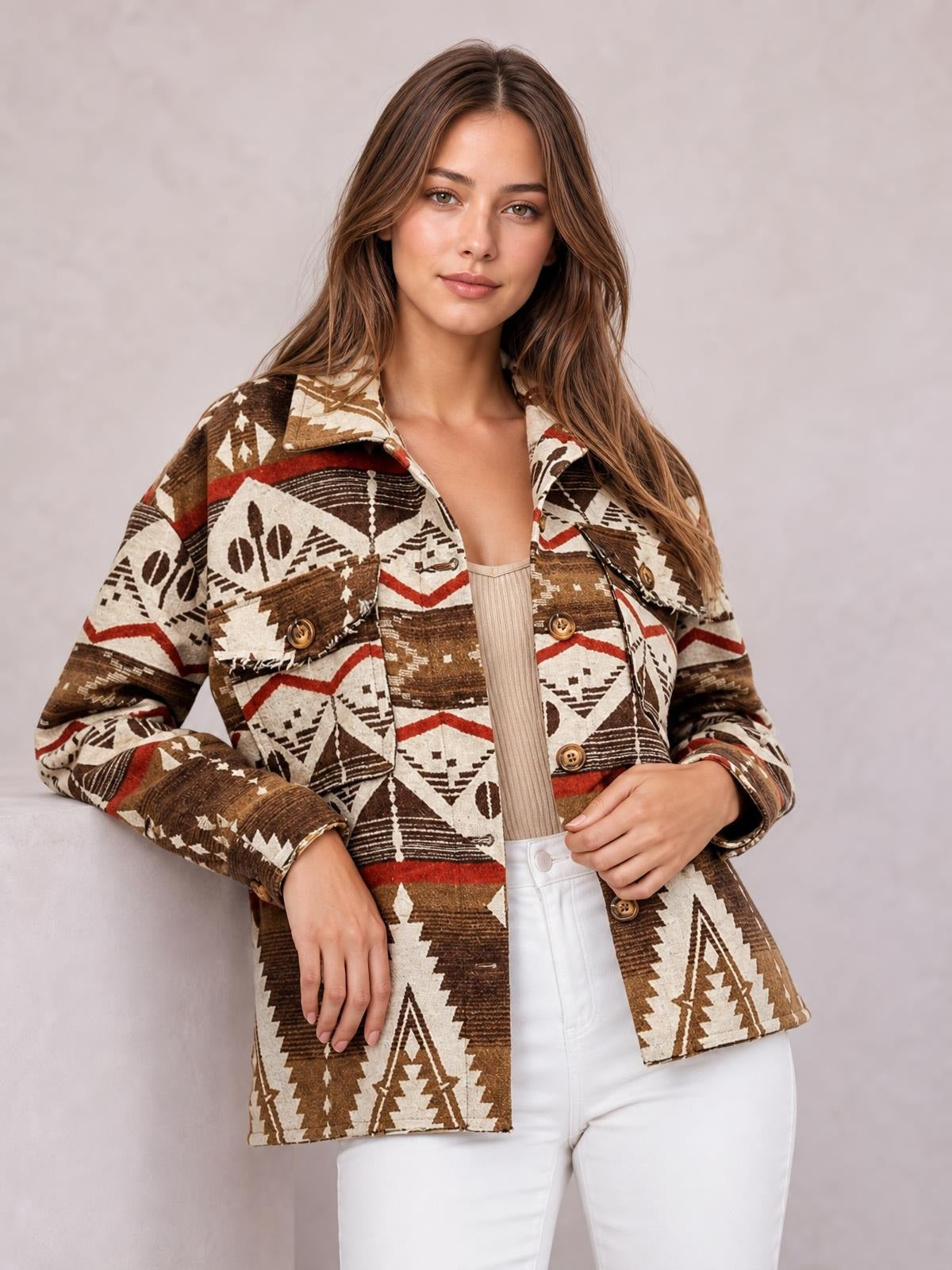 A woman poses wearing a brown, cream, and red geometric button-up jacket with long sleeves, a collar, chest pockets, and a relaxed silhouette.