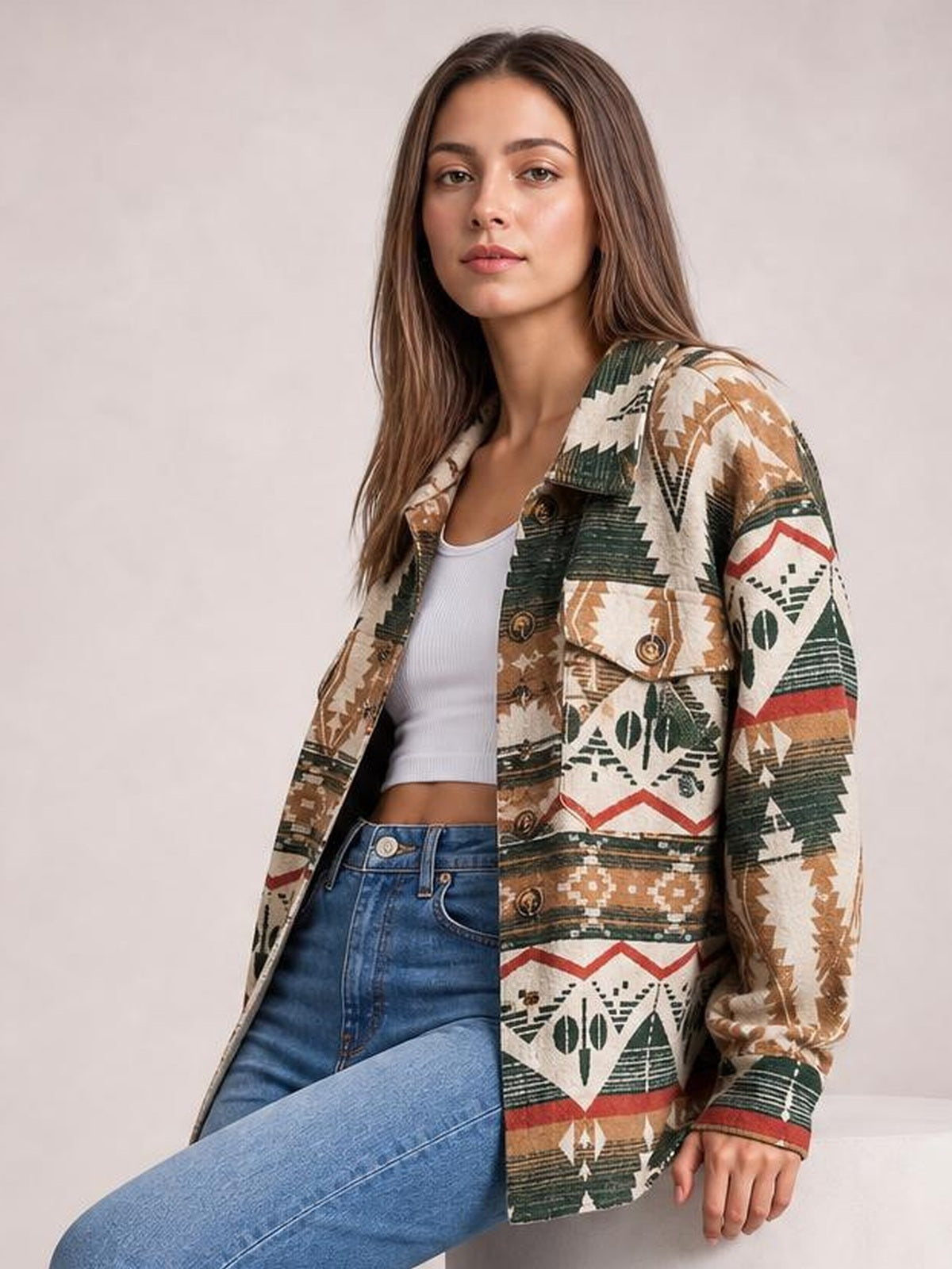 Model poses in a seated position wearing a long-sleeve geometric button-up jacket with earthy multicolor patterns, flap pockets, and a relaxed silhouette.