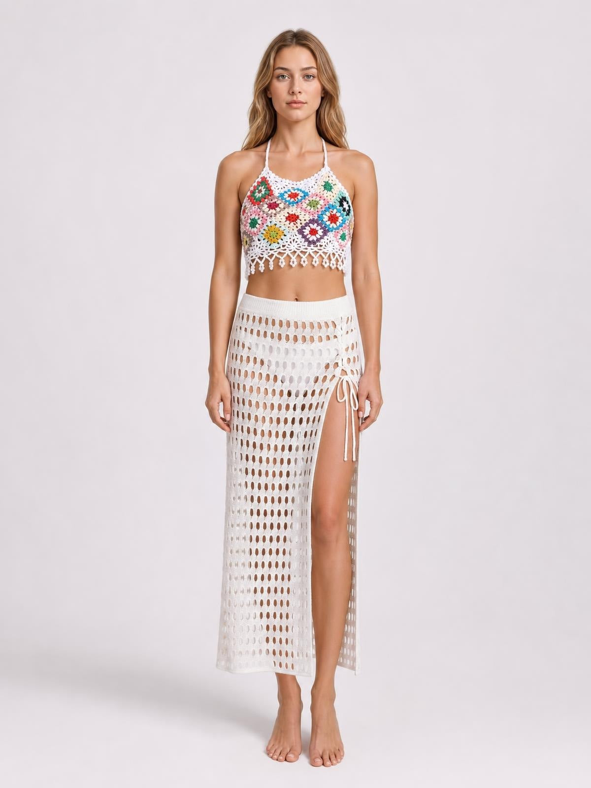 A model stands facing forward in a colorful geometric crochet halter neck swim top with thin straps, a cropped silhouette, and an openwork scalloped hem.