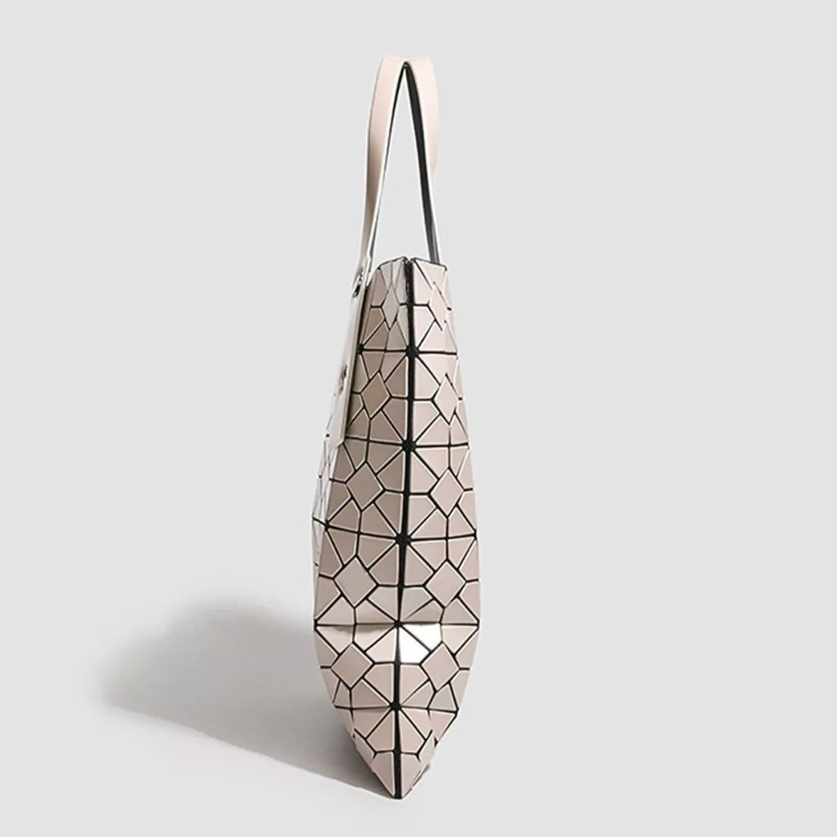 A medium PVC handbag with a pale blush geometric lattice pattern, long shoulder straps, and a structured tapered silhouette with pointed base.