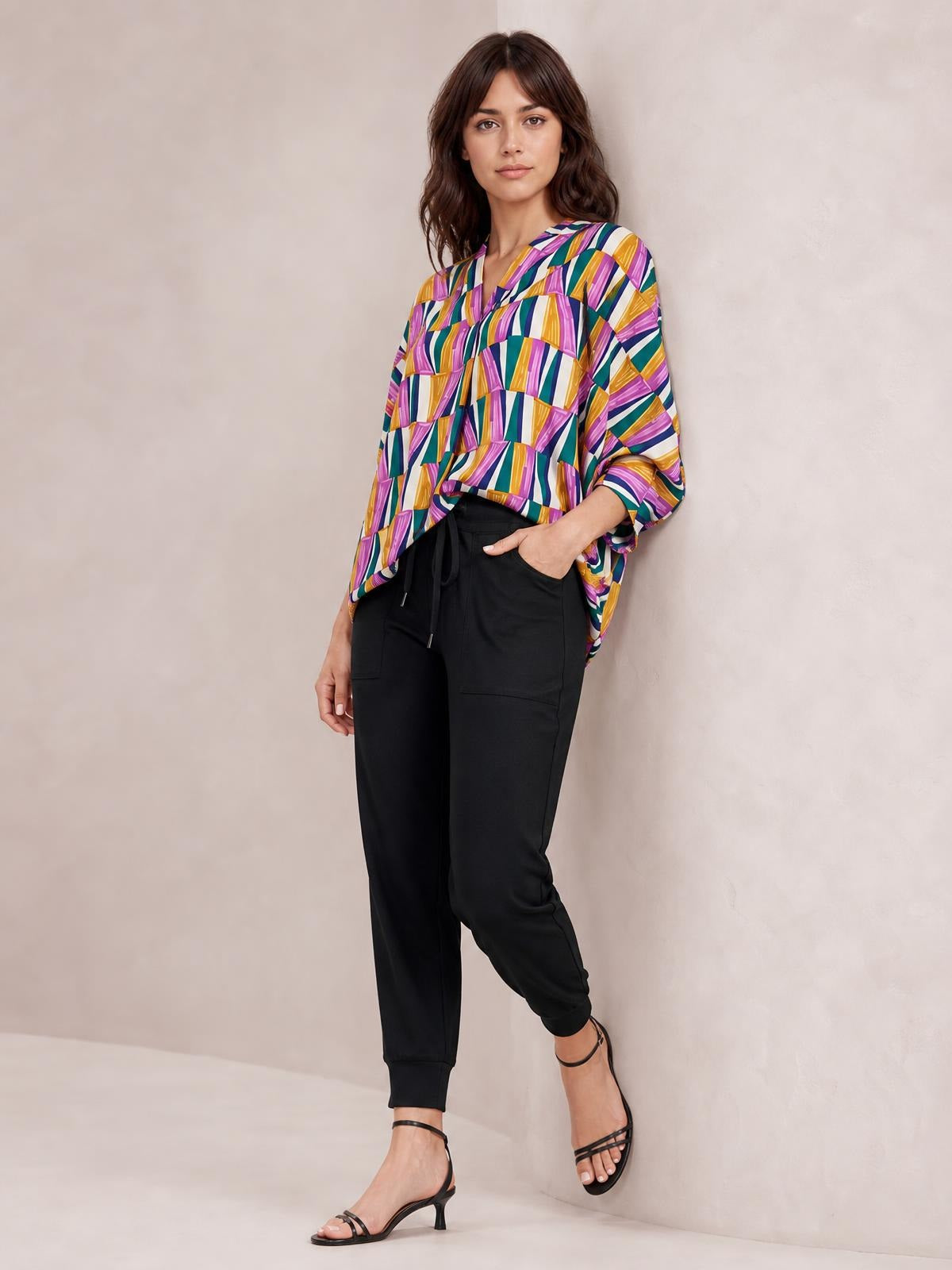 Model poses in a colorful geometric top with a notched neckline, relaxed dolman sleeves, and an easy draped silhouette.