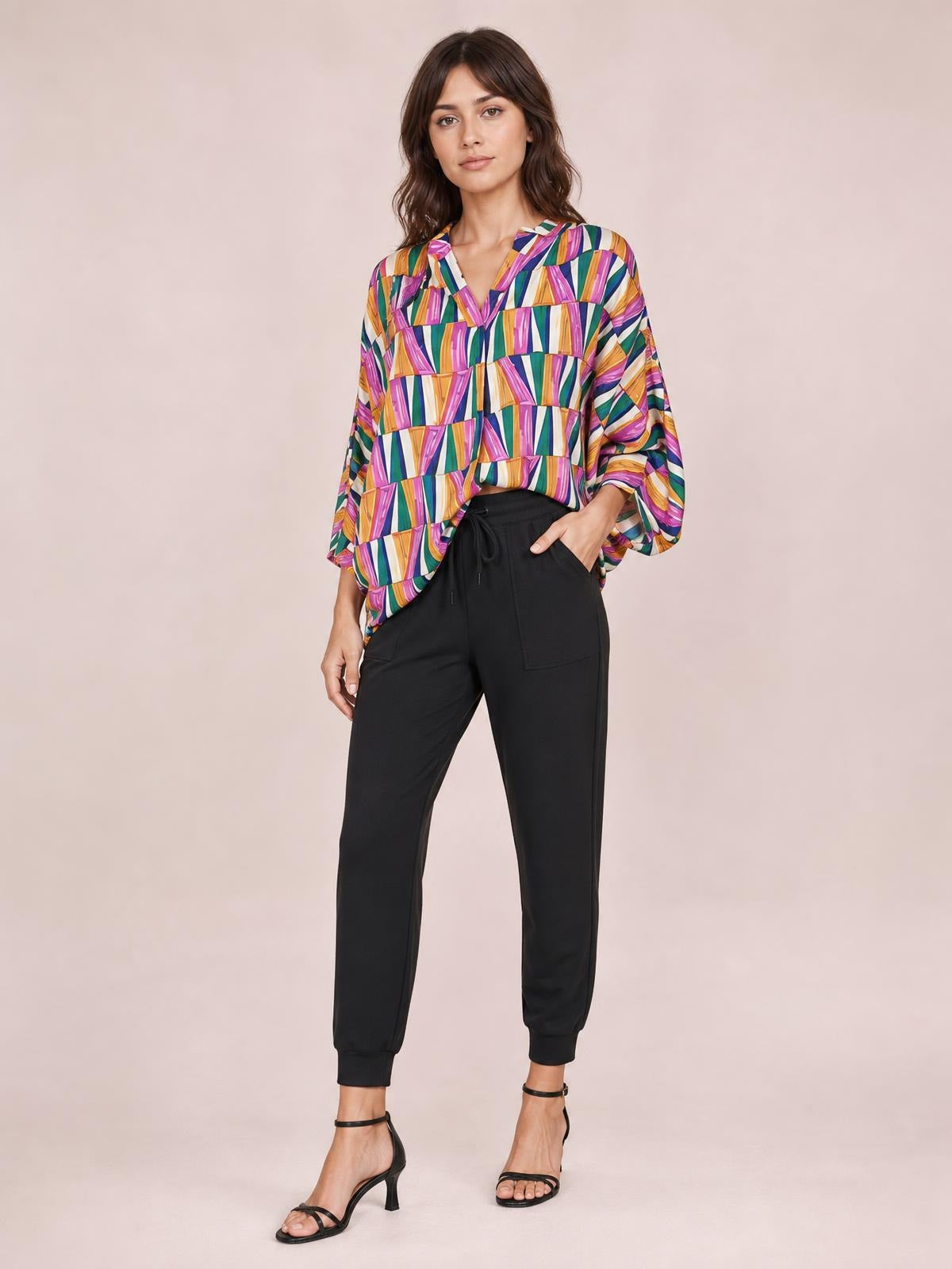 Model poses in a colorful geometric notched dolman sleeve top with a relaxed silhouette, loose long sleeves, and a curved hem.