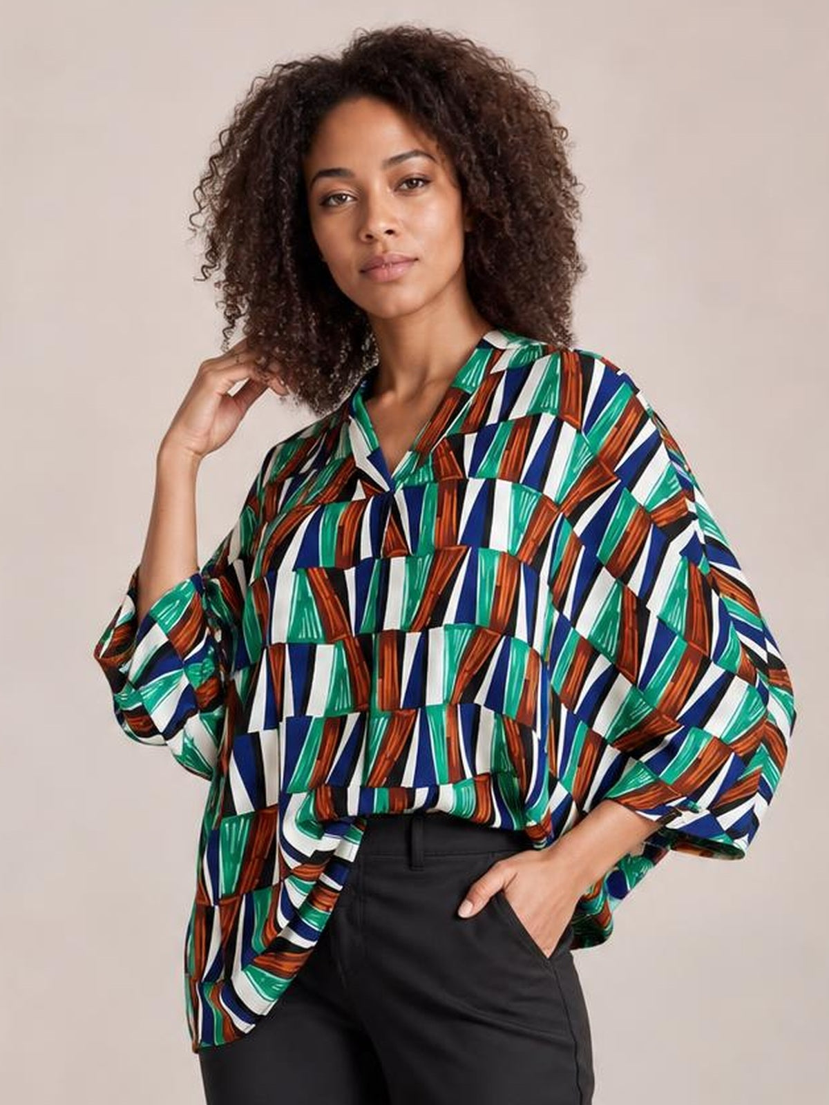 A model poses in a loose geometric top with a notched neckline and dolman sleeves, featuring bold green, blue, white, and rust stripes.