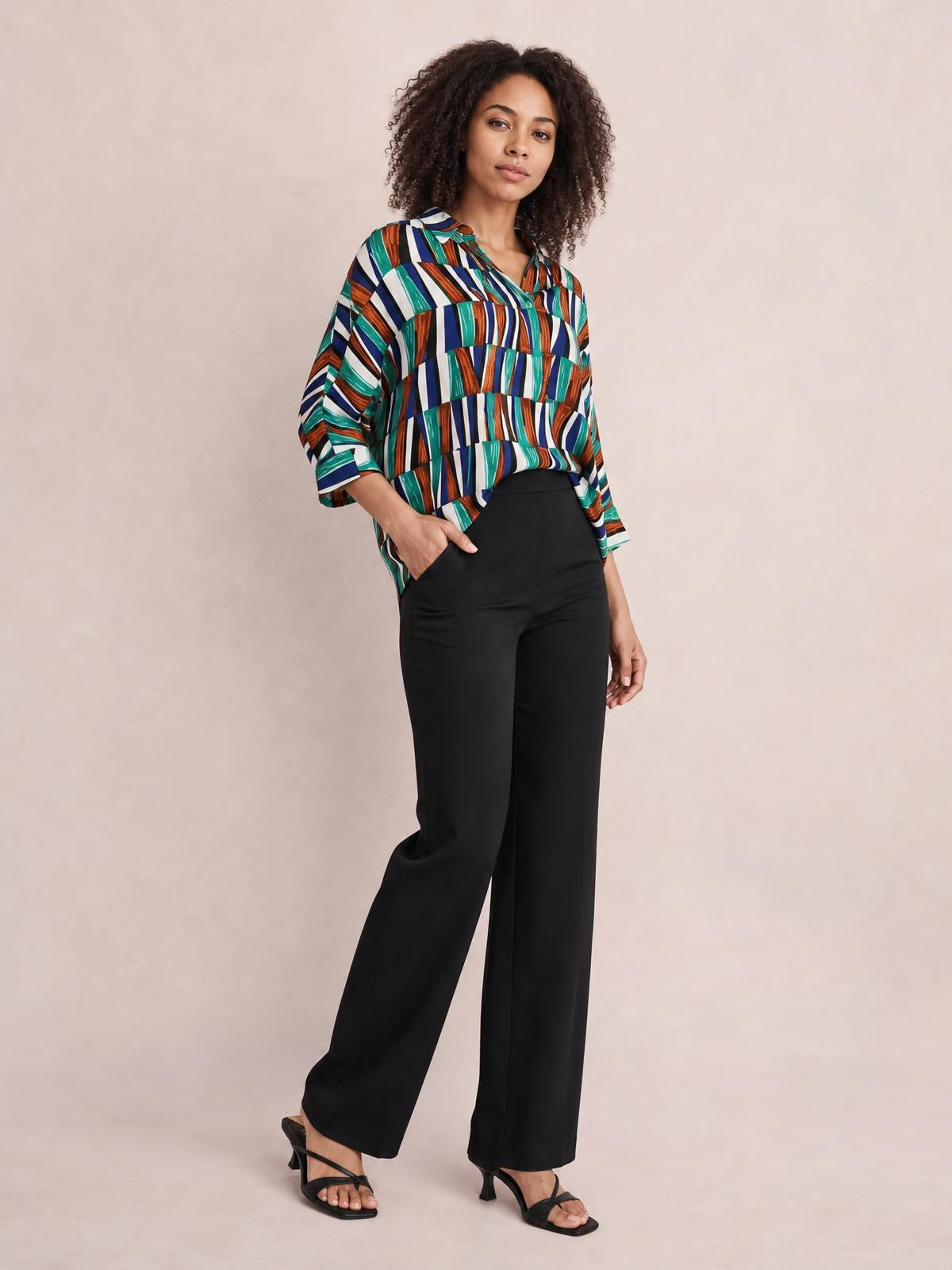 Model wearing a geometric multicolor notched top with loose dolman sleeves, a relaxed silhouette, and three-quarter cuffs, paired with black wide-leg pants.
