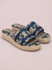 Geometric open-toe platform sandals with multicolored woven patterned uppers, navy braided straps, and thick natural-textured flat soles.