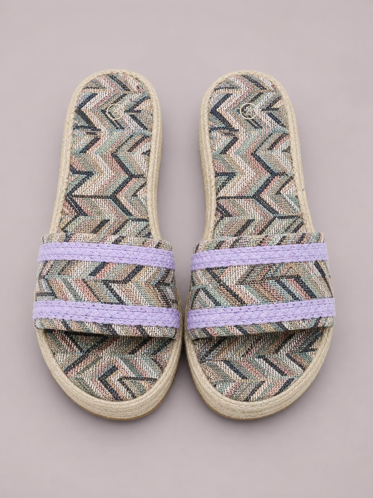 Geometric open-toe platform sandals feature a multicolor chevron-patterned upper, two lavender braided straps, and a flat rope-textured platform sole.