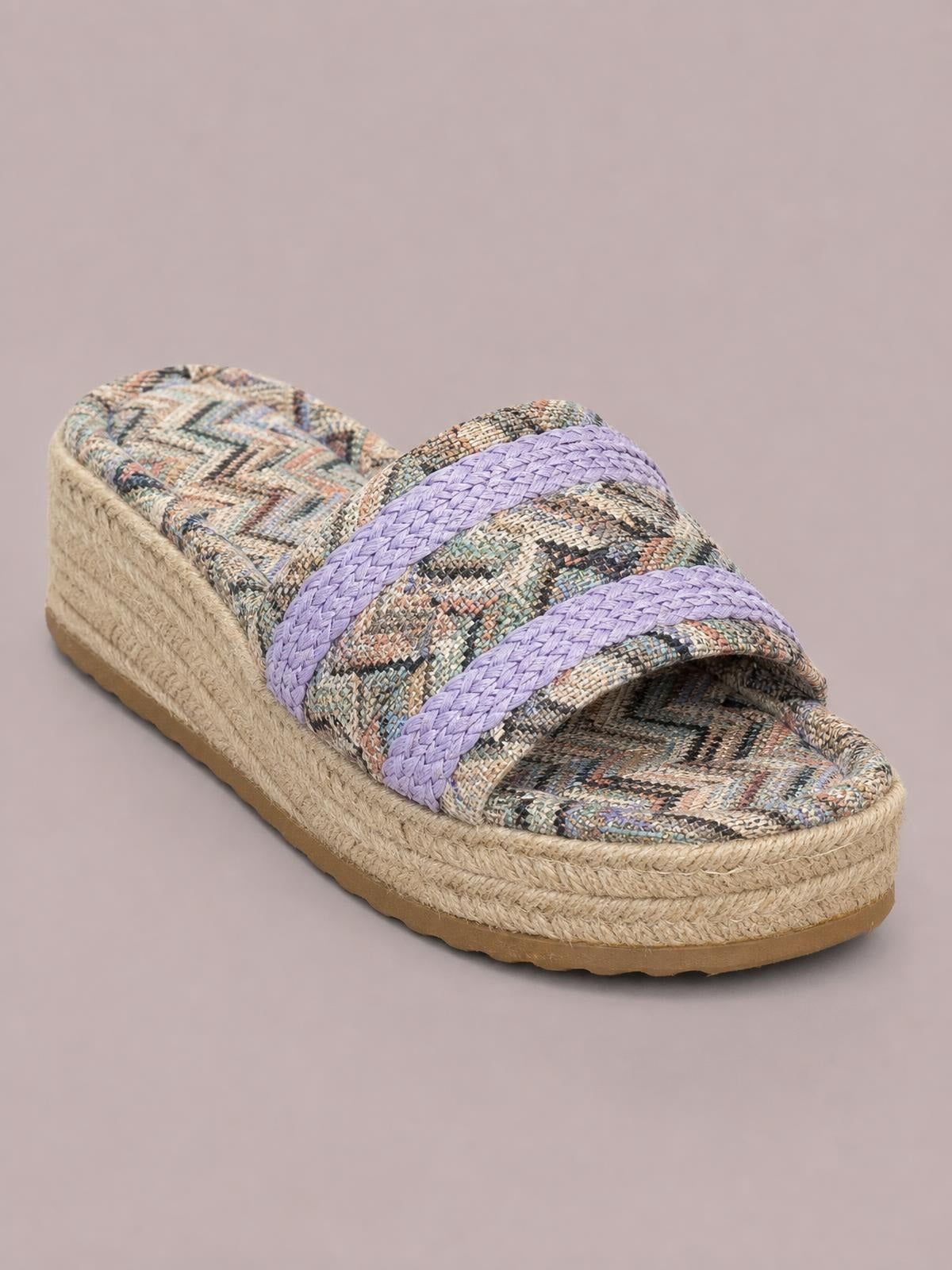 A geometric open-toe platform sandal features two lavender braided straps, a multicolored patterned footbed, and a textured beige wedge-style sole.