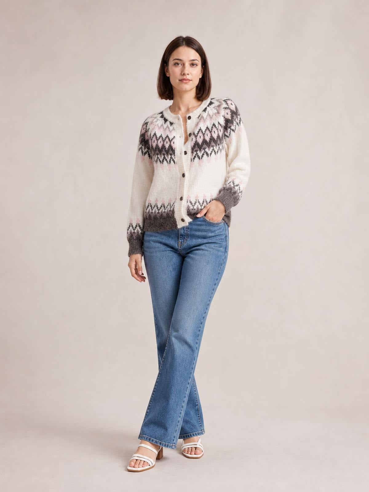 A woman poses in a cream brushed knit cardigan with geometric black and pink patterns, button front, round neck, ribbed cuffs and hem, and a relaxed silhouette.