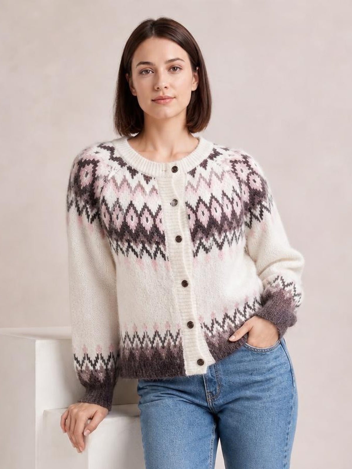 Model poses in blue jeans wearing a cream brushed knit cardigan with pink and dark geometric patterns, ribbed trim, long sleeves, and button-front construction.