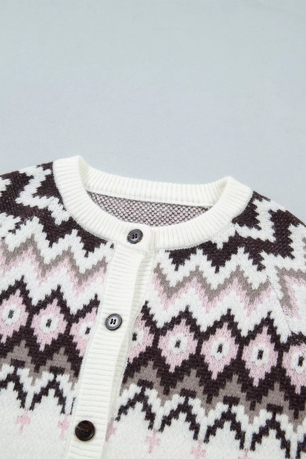Close-up of a brushed knit button cardigan in cream, black, gray, and pink geometric patterns, with a ribbed crew neckline, placket, and buttons.