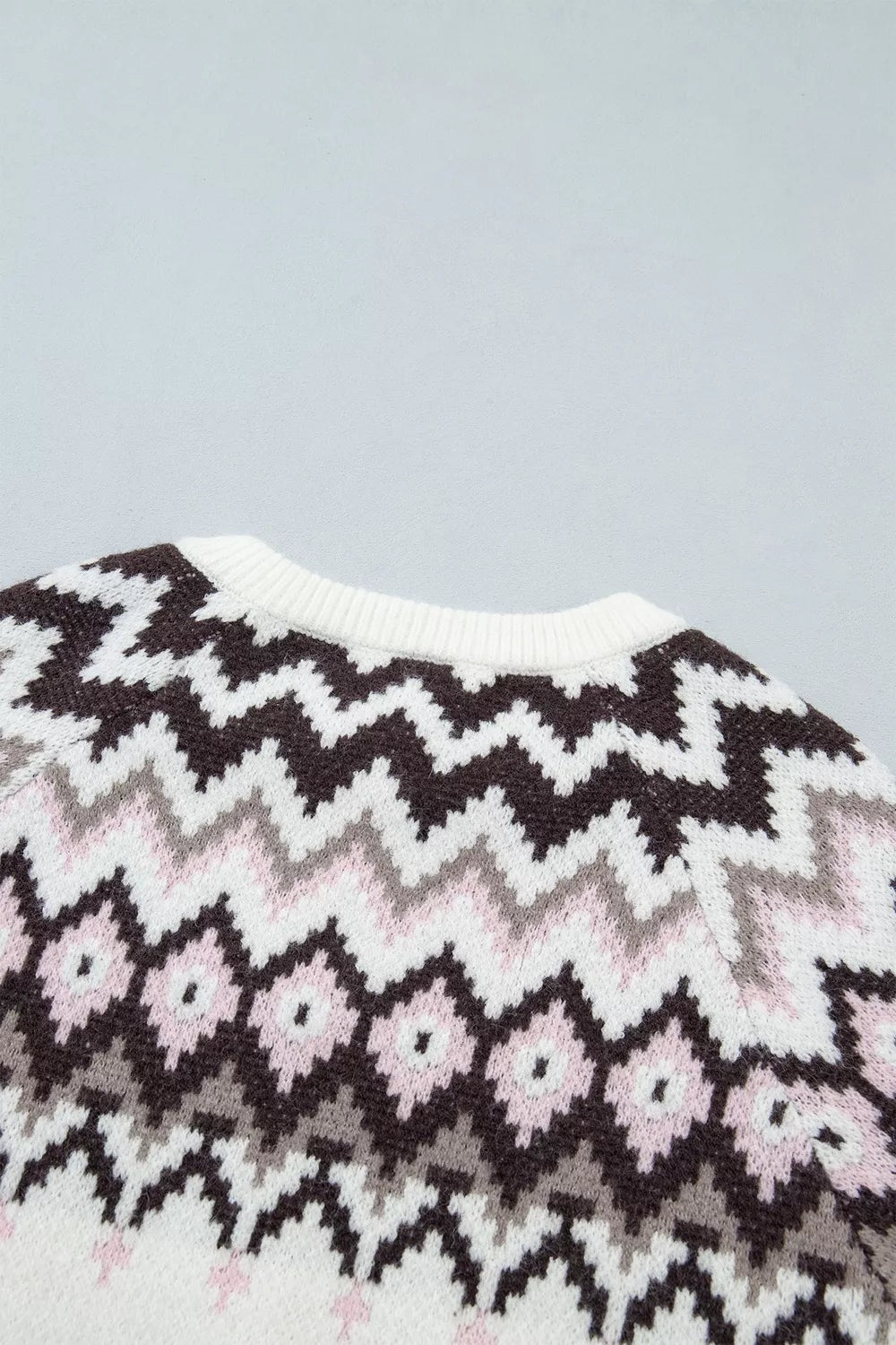 Close-up of a brushed knit cardigan featuring a white ribbed neckline and bold geometric zigzag and floral patterns in black, gray, and pale pink.