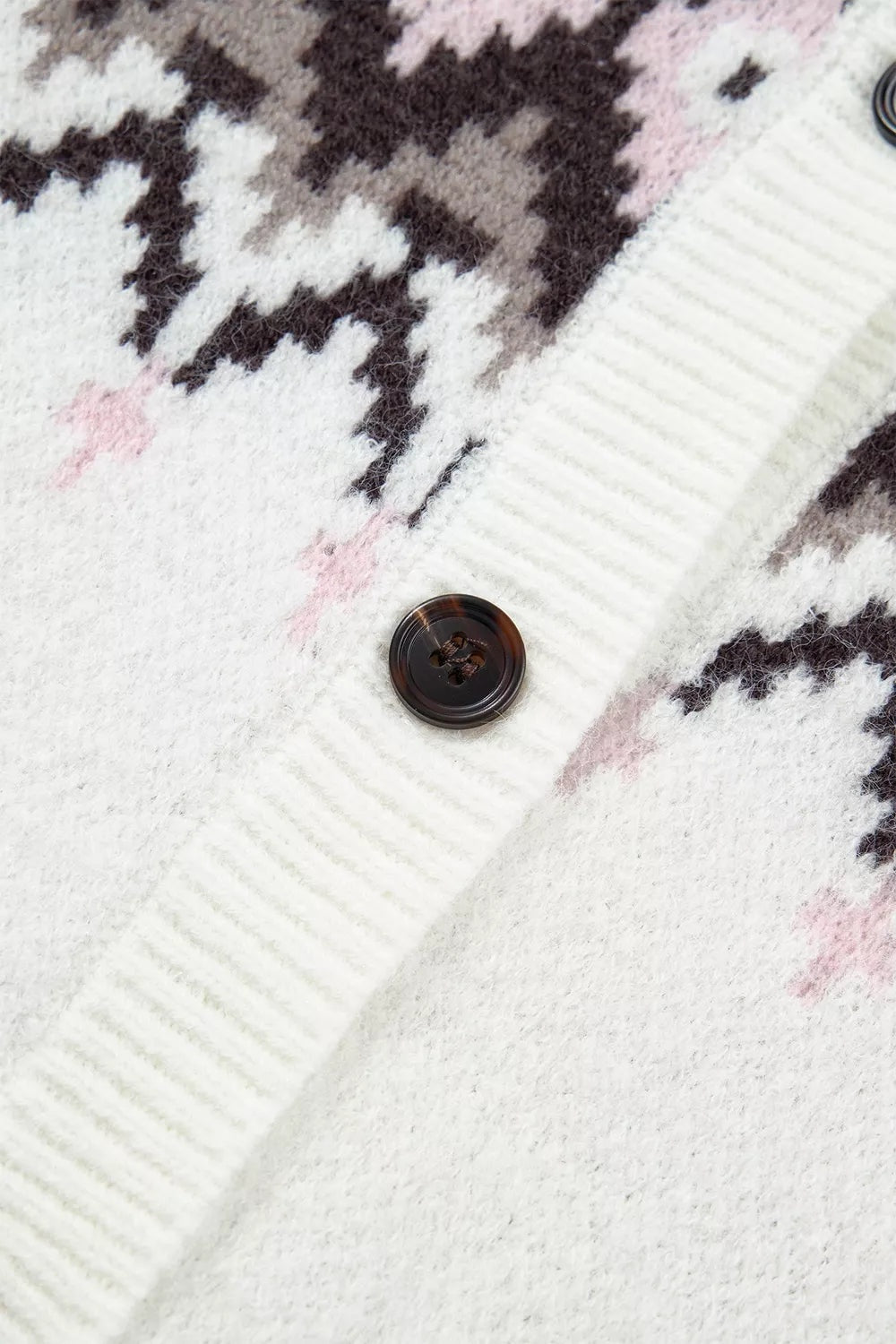 Close-up of a brushed knit cardigan showing its white geometric pattern, ribbed button placket, and dark four-hole button construction.