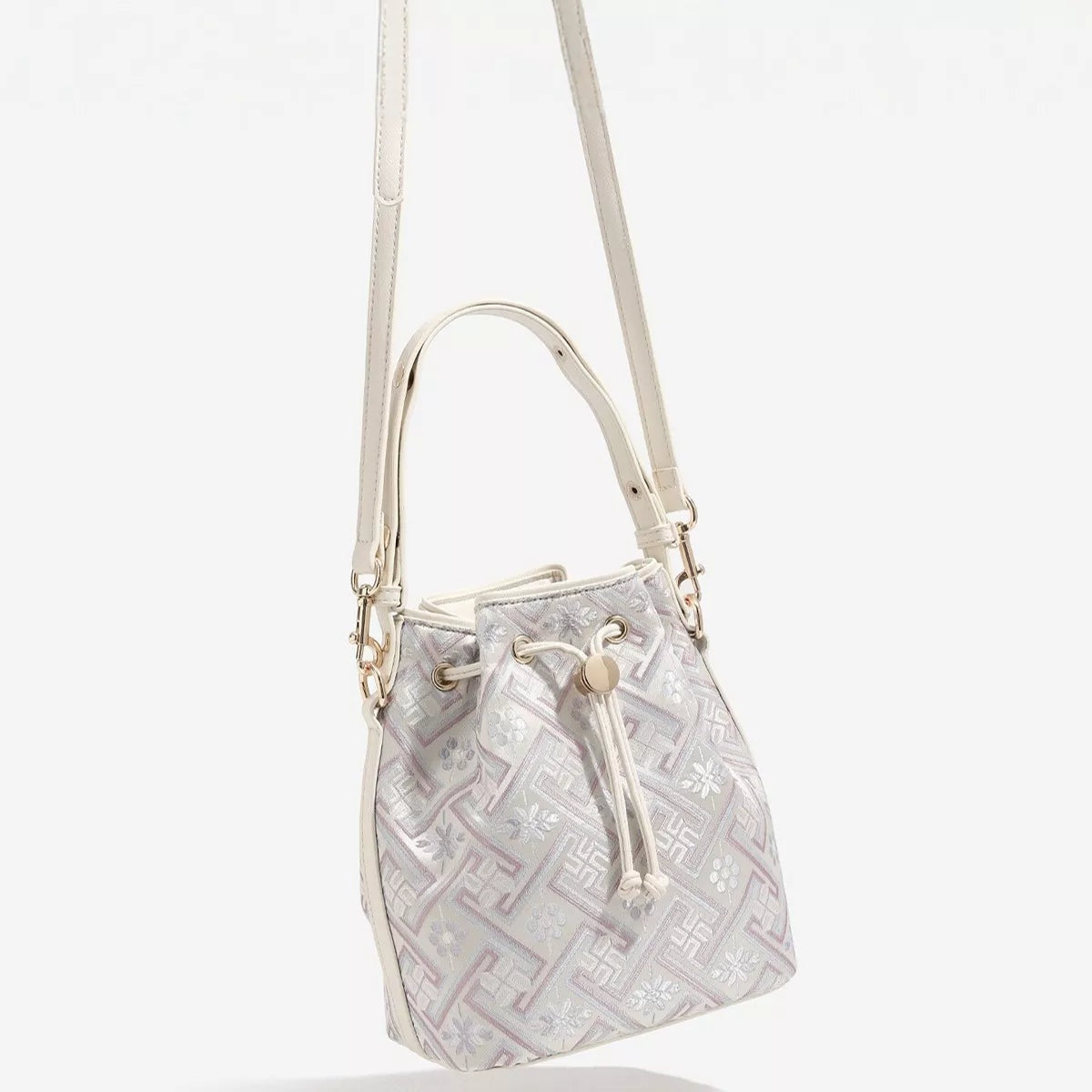 Small PU leather crossbody bucket bag in pale cream with a geometric patterned body, drawstring closure, structured base, and adjustable strap.