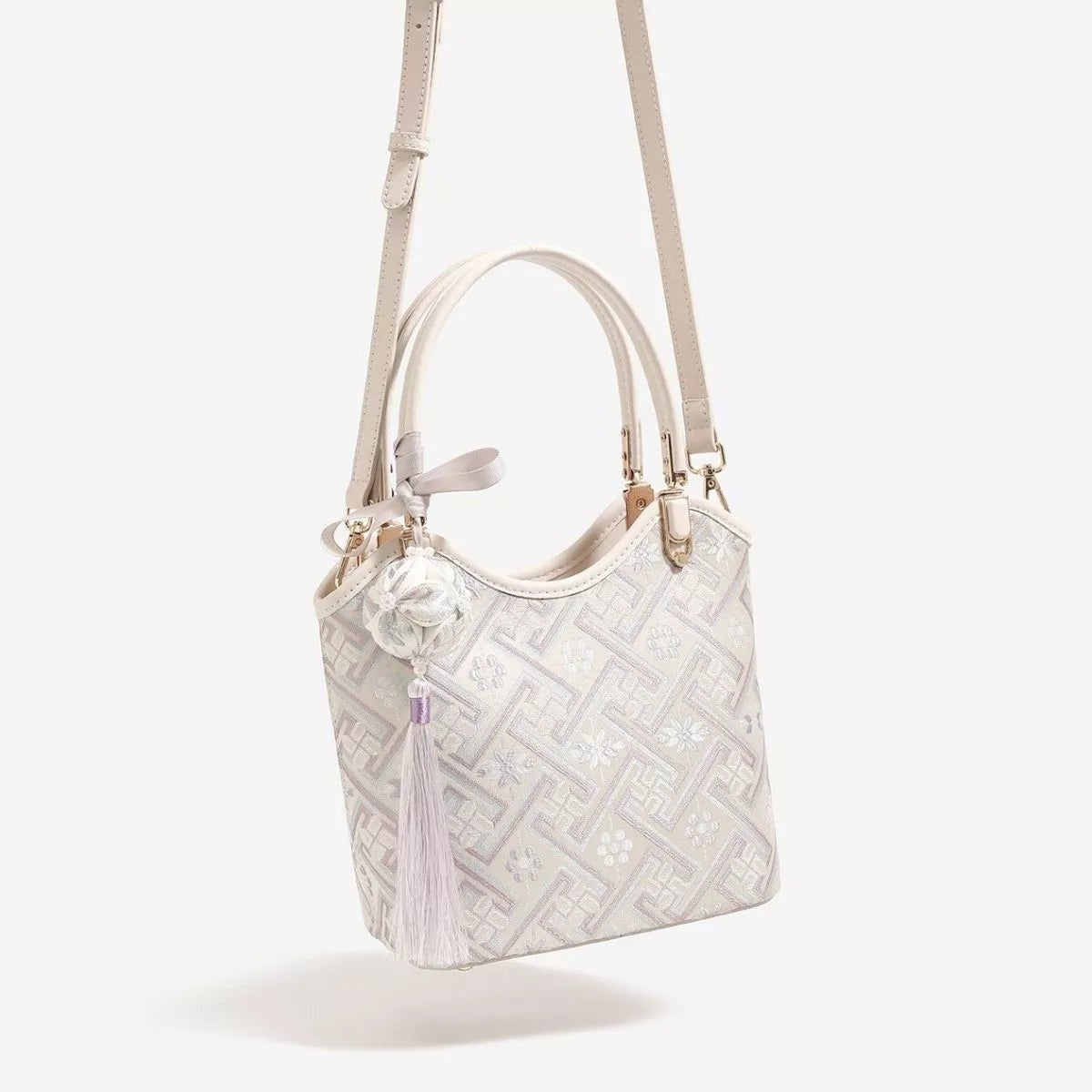 Small ivory polyester handbag with a geometric patterned body, floral accents, double top handles, and a long adjustable shoulder strap.