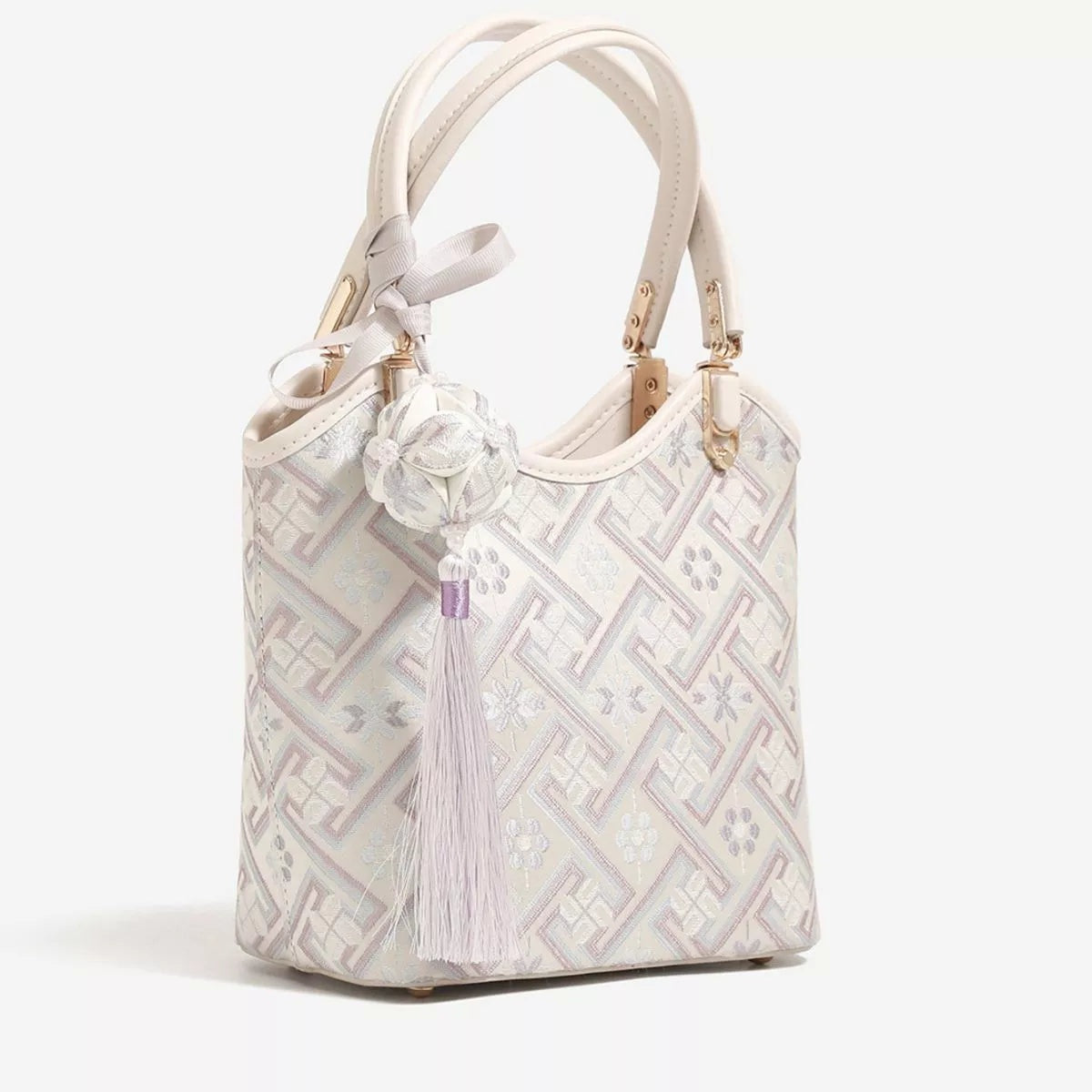 Small cream polyester handbag with a geometric pattern, rounded bucket silhouette, twin top handles, gold-tone hardware, and a long decorative tassel.