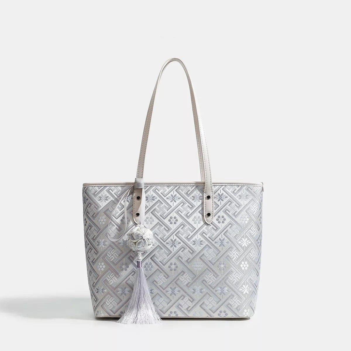 Medium structured faux leather tote bag in white and silver with a geometric pattern, twin long shoulder straps, stitched trim, and a rectangular silhouette.