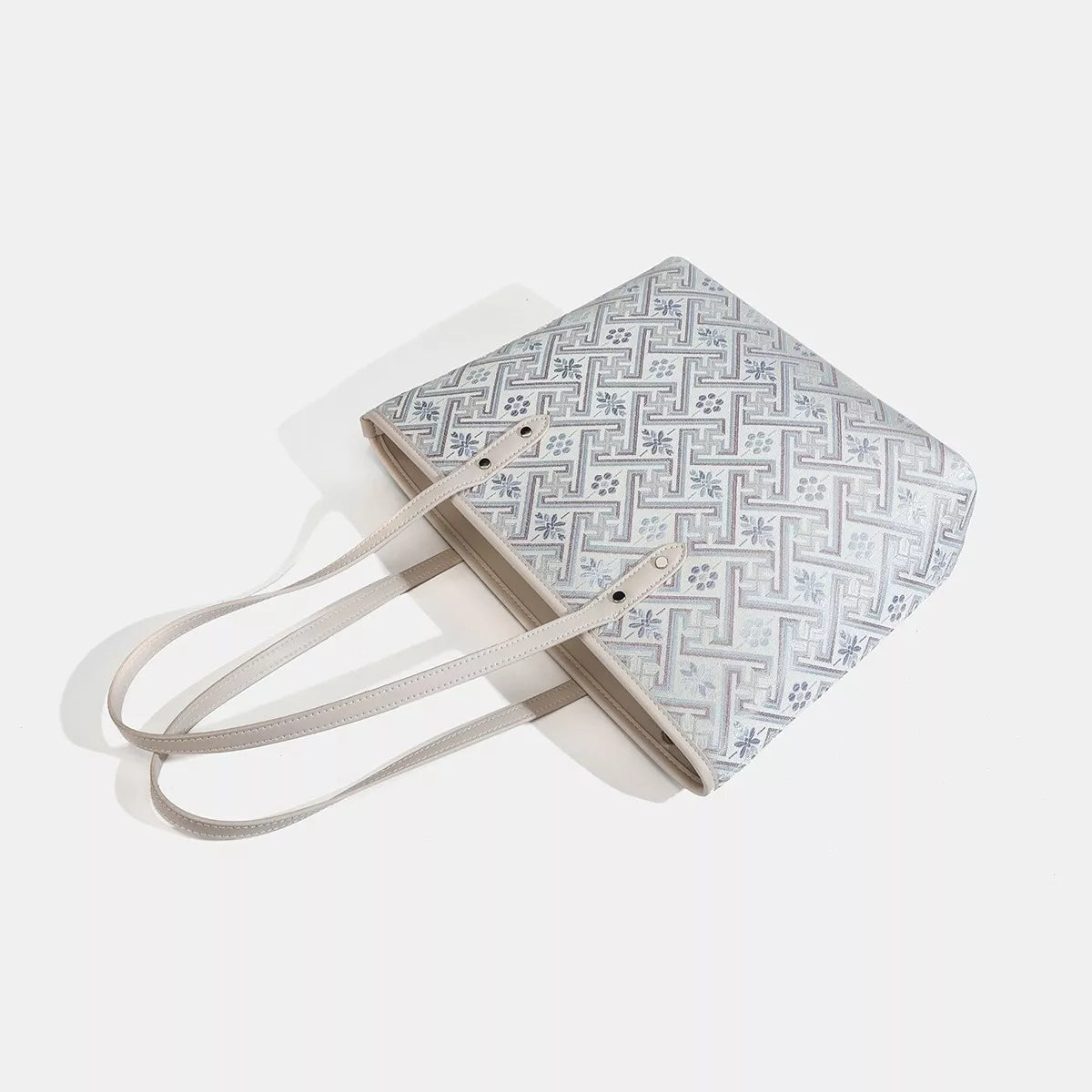 Medium faux leather tote bag with a light geometric pattern, structured rectangular silhouette, and two long top handles in a soft gray finish.