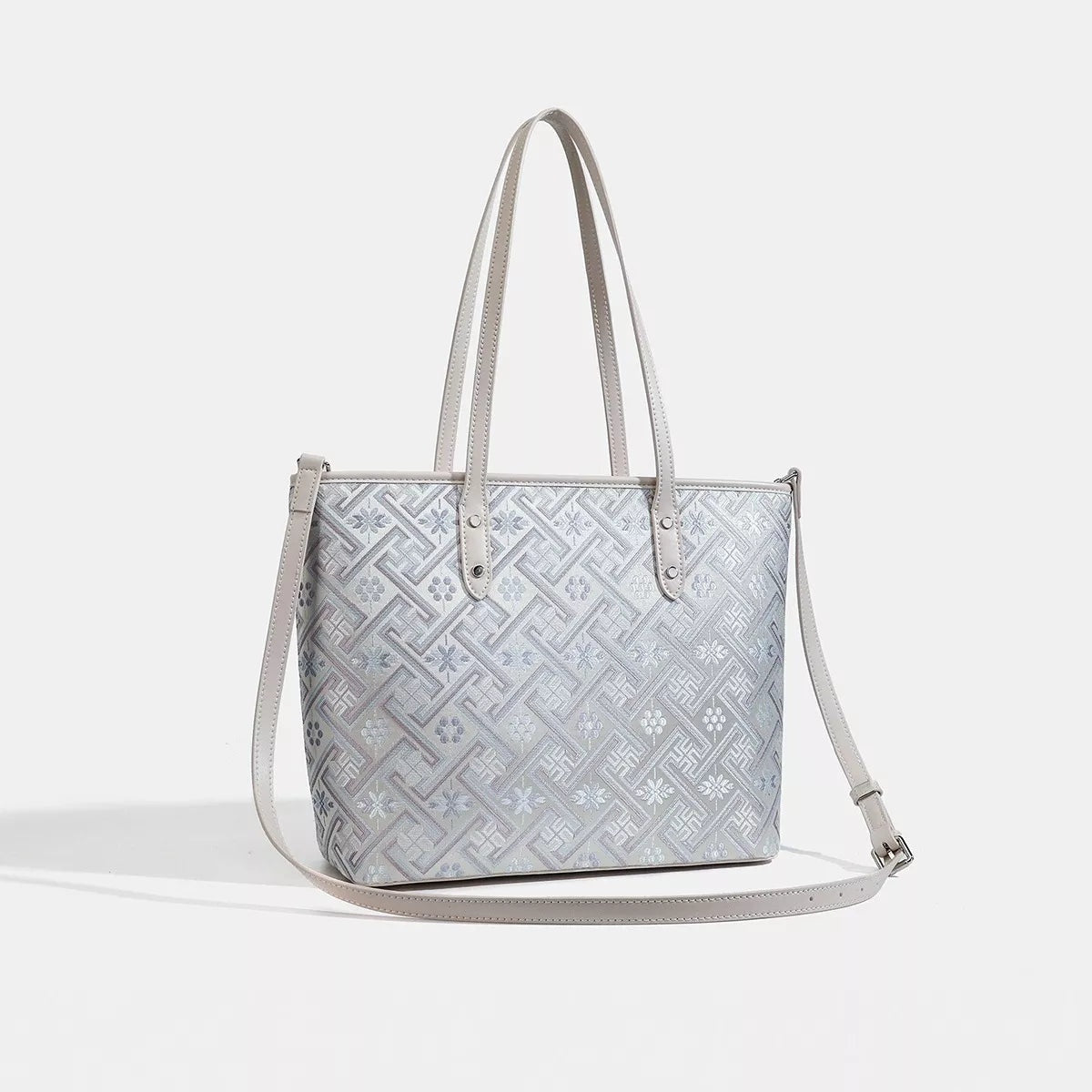 Medium faux leather geometric pattern tote bag in light gray and white, featuring a structured rectangular silhouette, twin top handles, and a long adjustable shoulder strap.