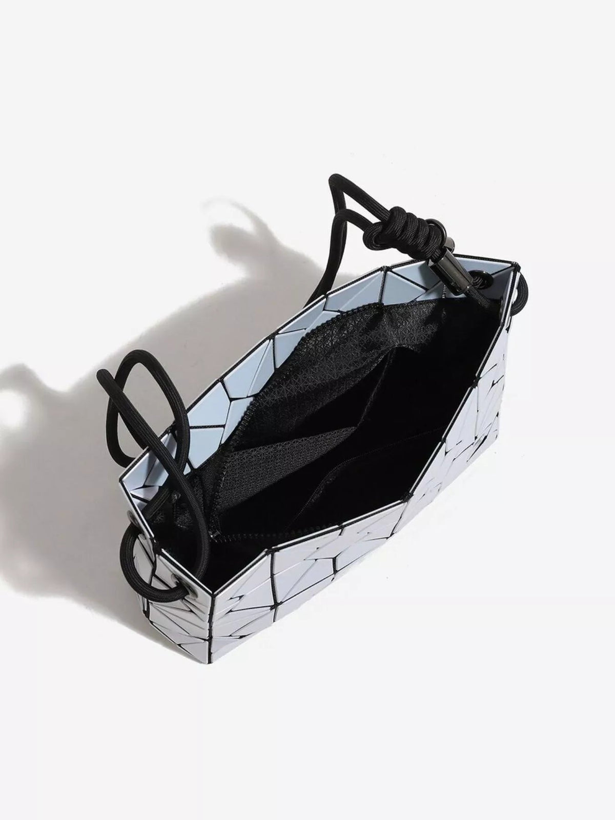Small PVC shoulder bag with a geometric prism silhouette, iridescent reflective panels, open top, black rope handles, and a structured black-lined interior.