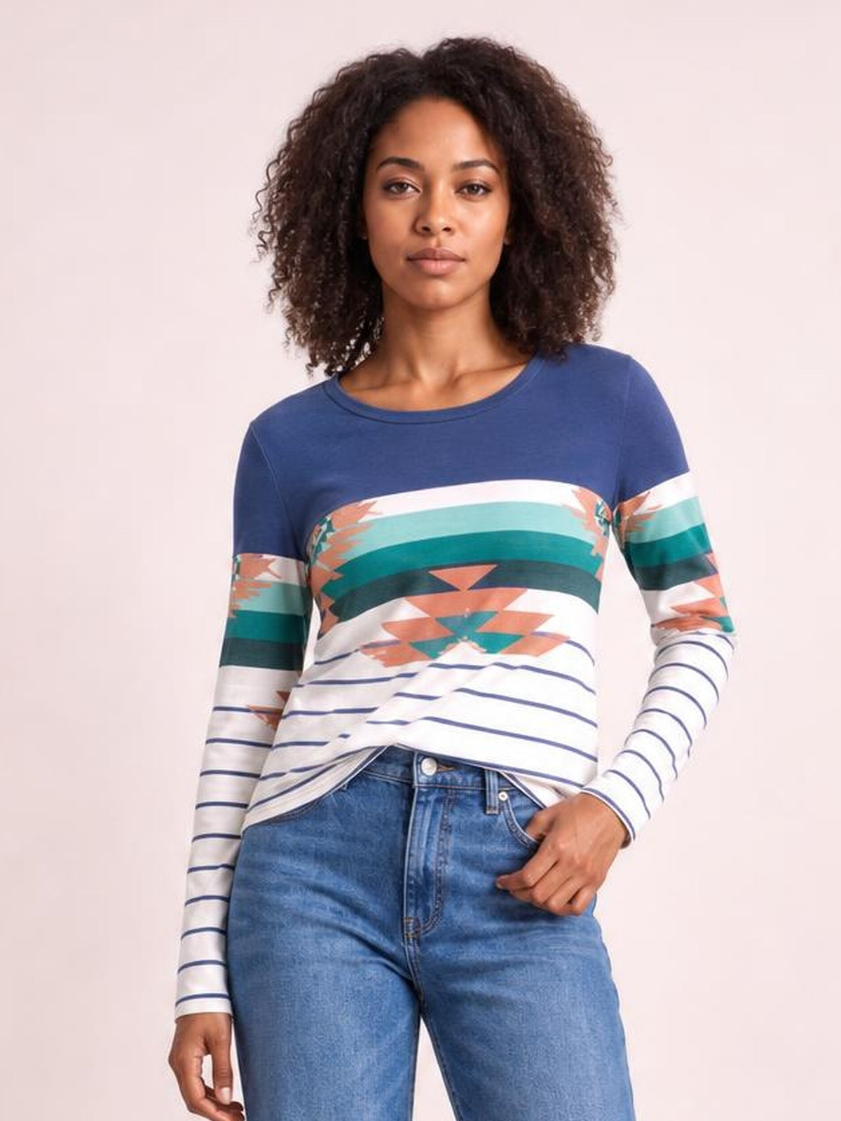 Model wearing a navy geometric round neck long sleeve T-shirt with multicolor striped and abstract print, fitted silhouette, and one hand resting in a jeans pocket.
