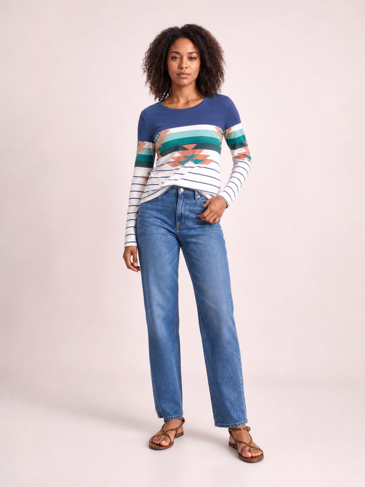 Model wears a geometric round neck long sleeve T-shirt with a blue base, colorful patterned bands, striped sleeves, and a relaxed straight silhouette.