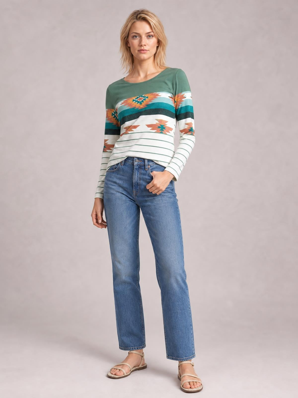 Model in a relaxed standing pose wears a green geometric round-neck long-sleeve T-shirt with colorful patterned bands and a straight silhouette.