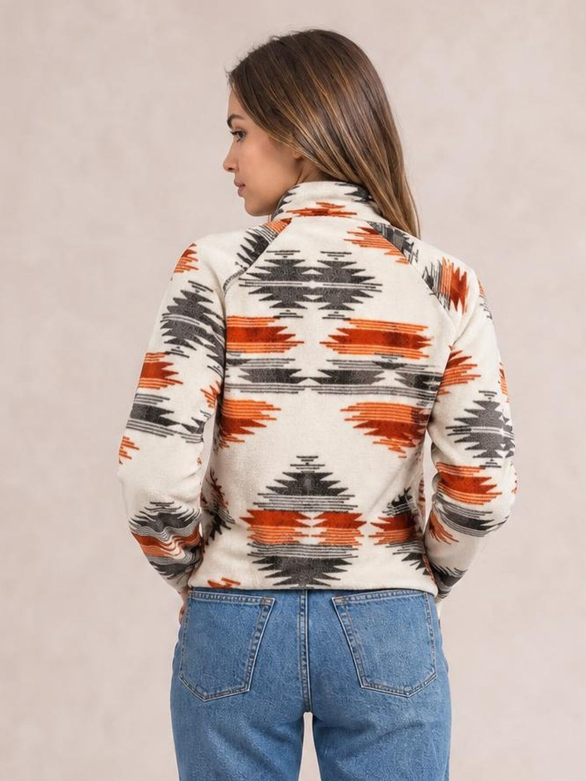 A woman poses with her back turned, showing a cream Geometric Snap Down Jacket with rust and charcoal geometric motifs, long sleeves, and a neat silhouette.