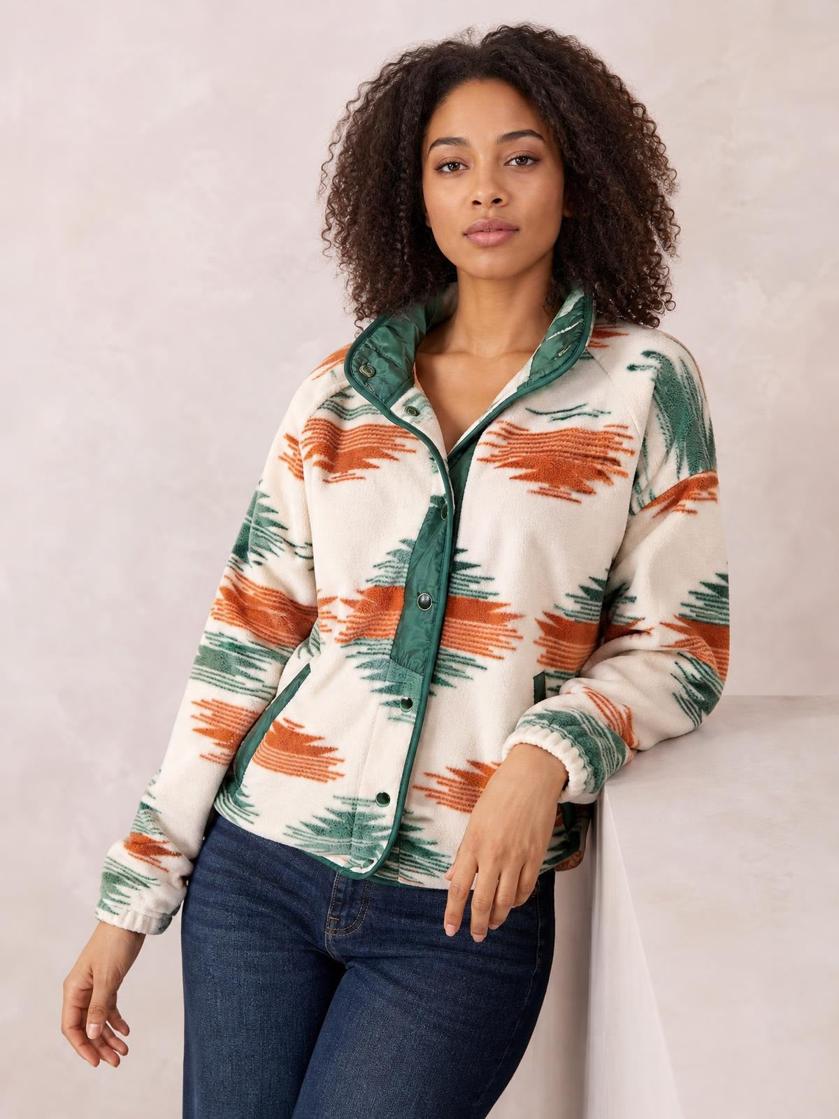 A woman wears a cream geometric snap-down jacket with orange and green patterned stripes, contrast green trim, a high collar, long sleeves, and front pockets.