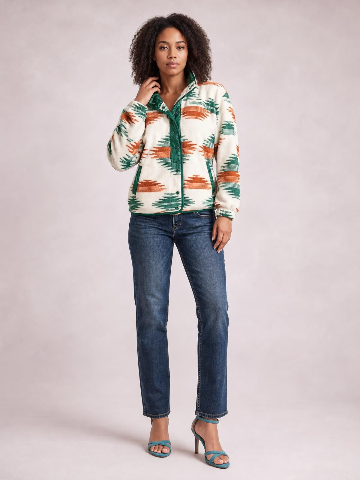 A model poses in a cream Geometric Snap Down Jacket with rust and green patterns, snap front, collar, pockets, relaxed silhouette, and one hand at the collar.