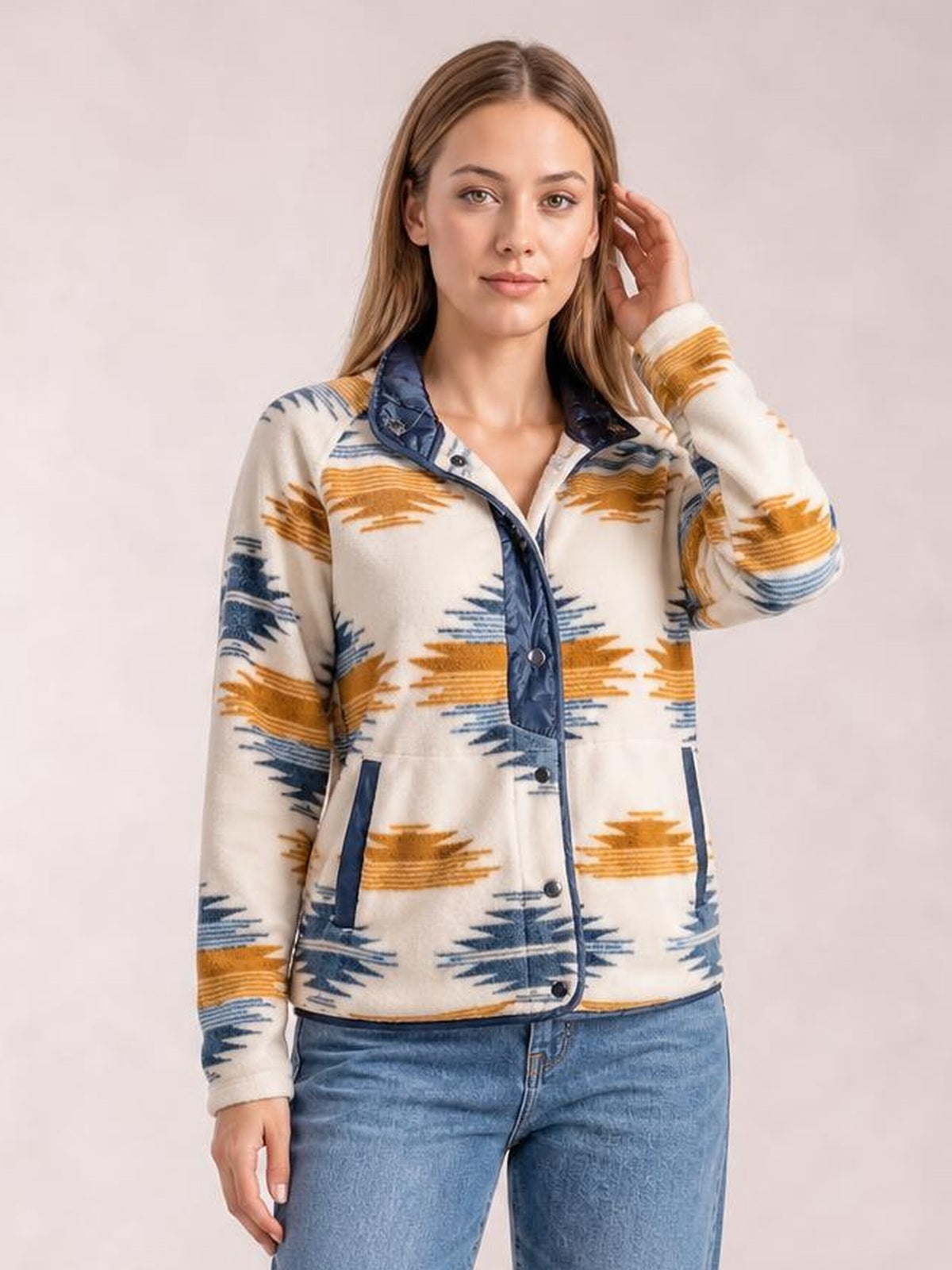A model poses in a cream geometric snap-down jacket with navy and mustard patterns, contrast trim, long sleeves, front pockets, and a collared silhouette.