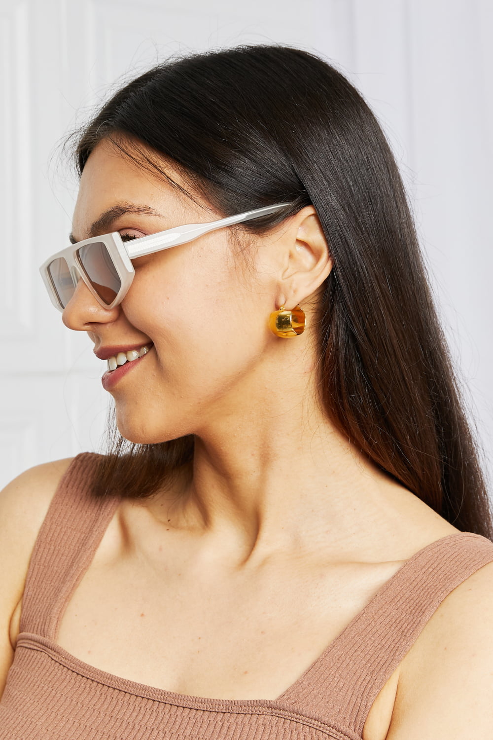 Smiling model in side profile wears warm caramel geometric acetate sunglasses with a structured rectangular silhouette and tinted TAC polarized lenses.
