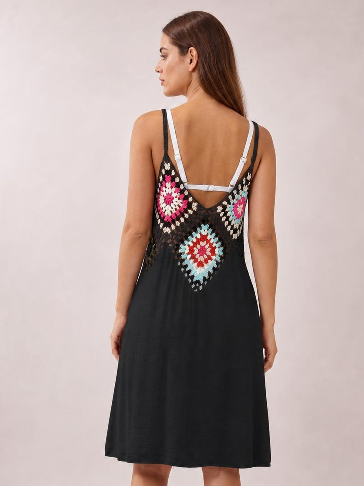 A model stands facing away in a black geometric V-neck spaghetti strap cover-up dress with a colorful patterned bodice and flowing A-line silhouette.