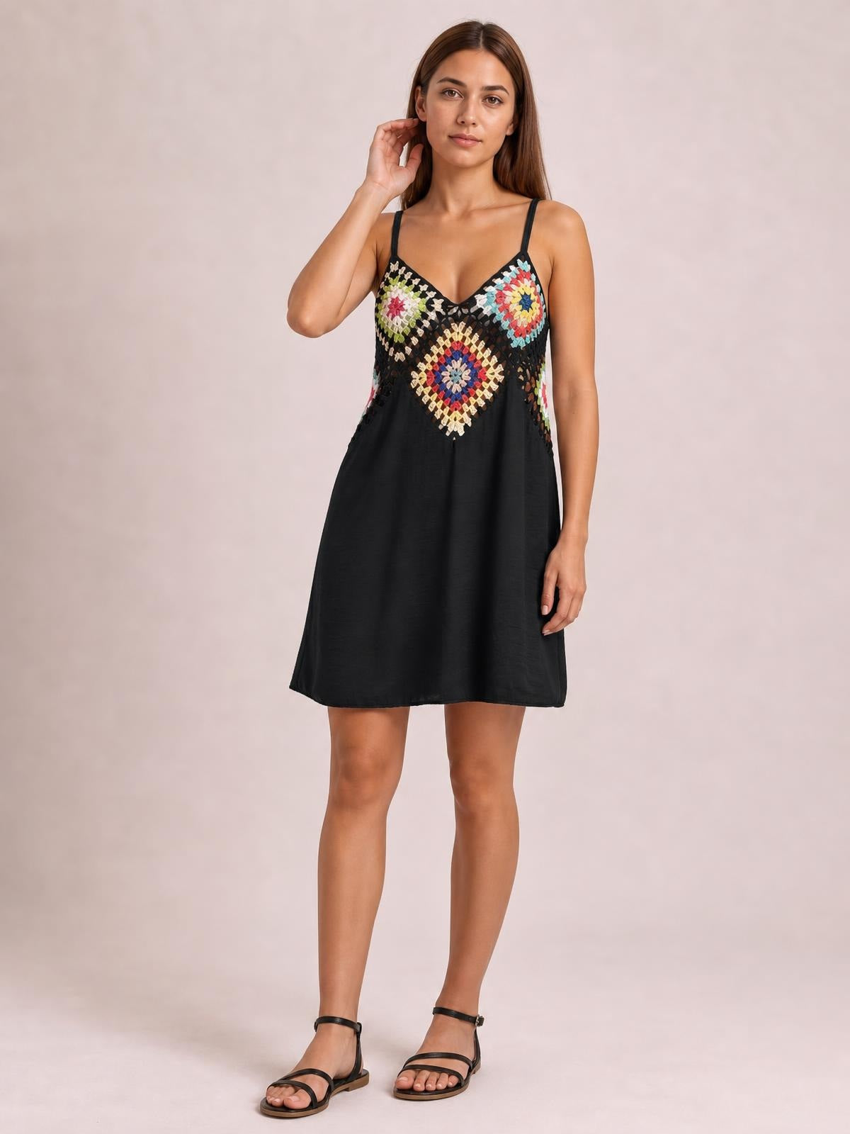 A model stands with one hand near her hair wearing a black geometric V-neck spaghetti strap cover-up dress with a flared mini silhouette.