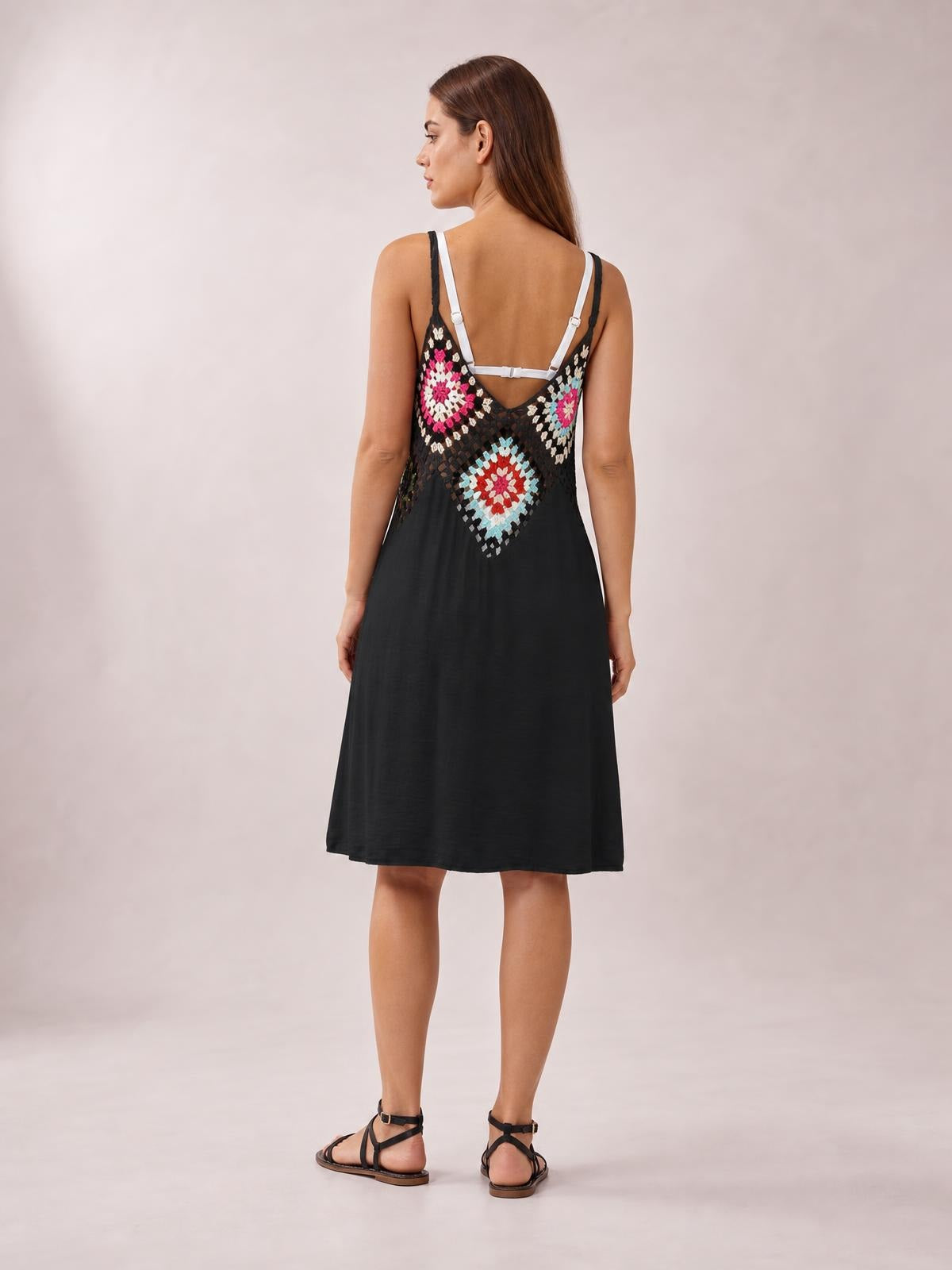 A model stands facing away in a black geometric spaghetti strap cover up dress with a semi-sheer patterned bodice and relaxed, flowing A-line silhouette.