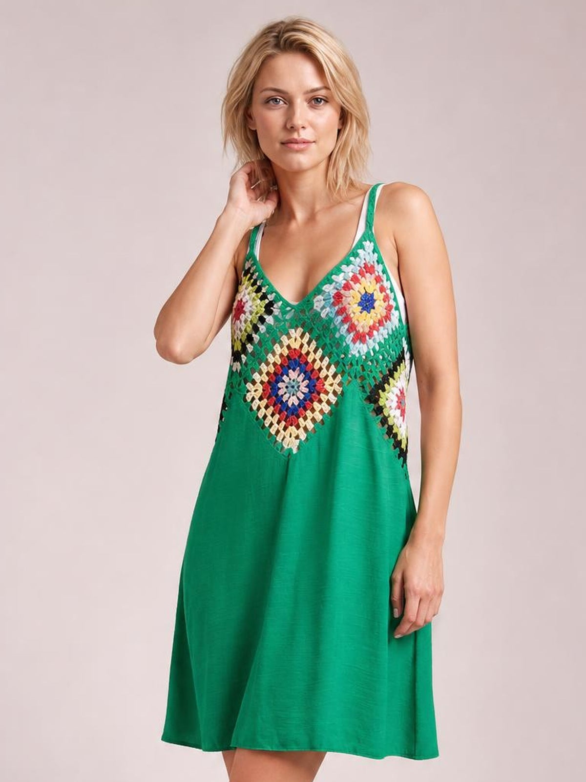 A model touches her neck while wearing a green geometric V-neck spaghetti-strap cover-up dress with a colorful patterned bodice and flowing A-line silhouette.