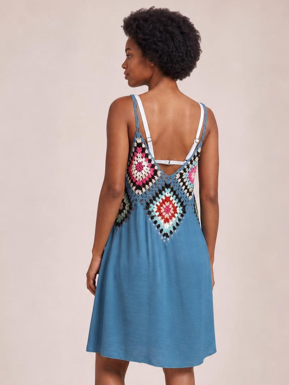 Model seen from behind wearing a blue geometric V-neck spaghetti-strap cover-up dress with a low back, colorful patterned yoke, and relaxed A-line silhouette.