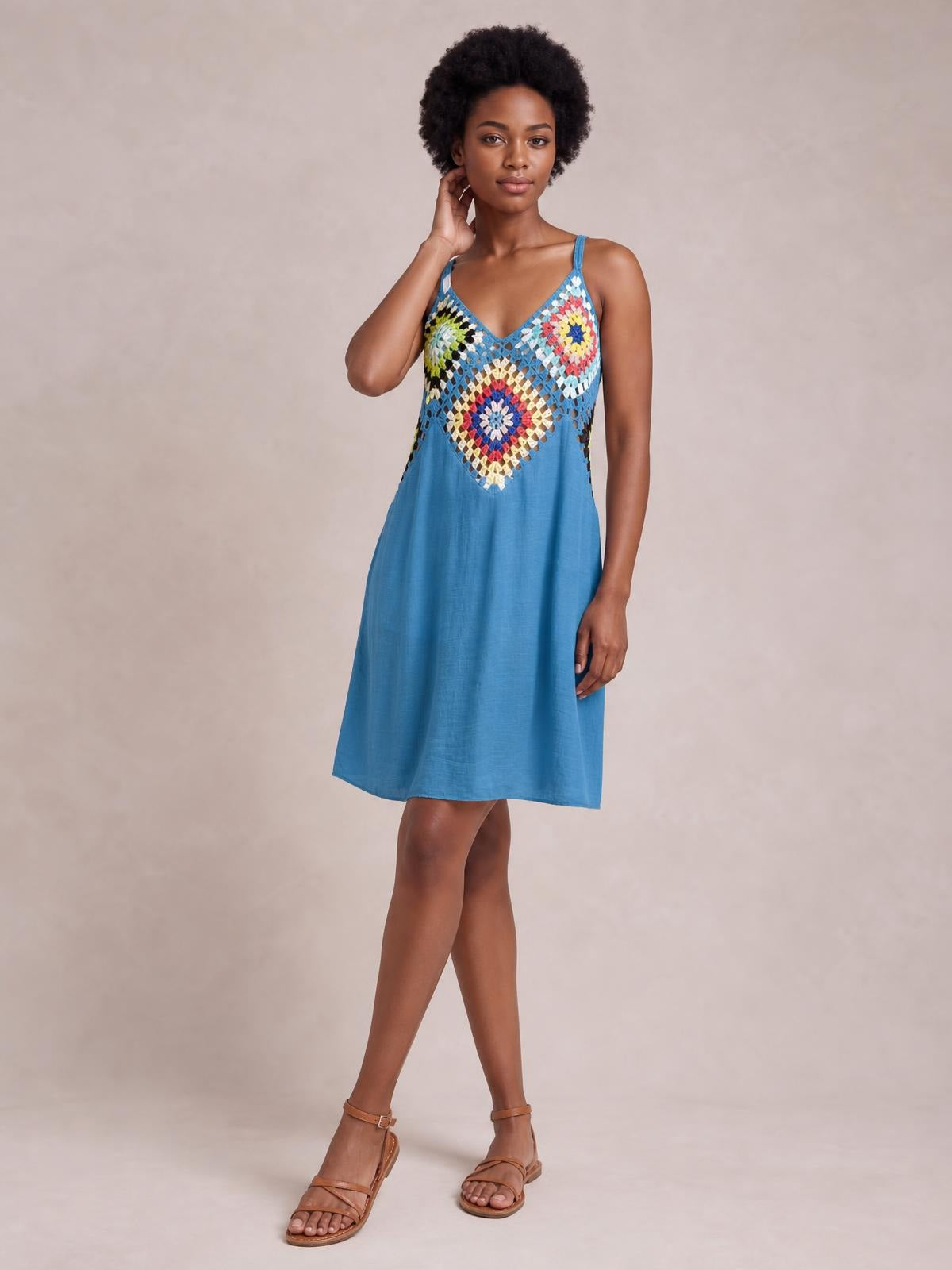 Model wears a blue geometric V-neck spaghetti strap cover-up dress with a semi-sheer patterned bodice and relaxed A-line silhouette, posing with one hand at her neck.