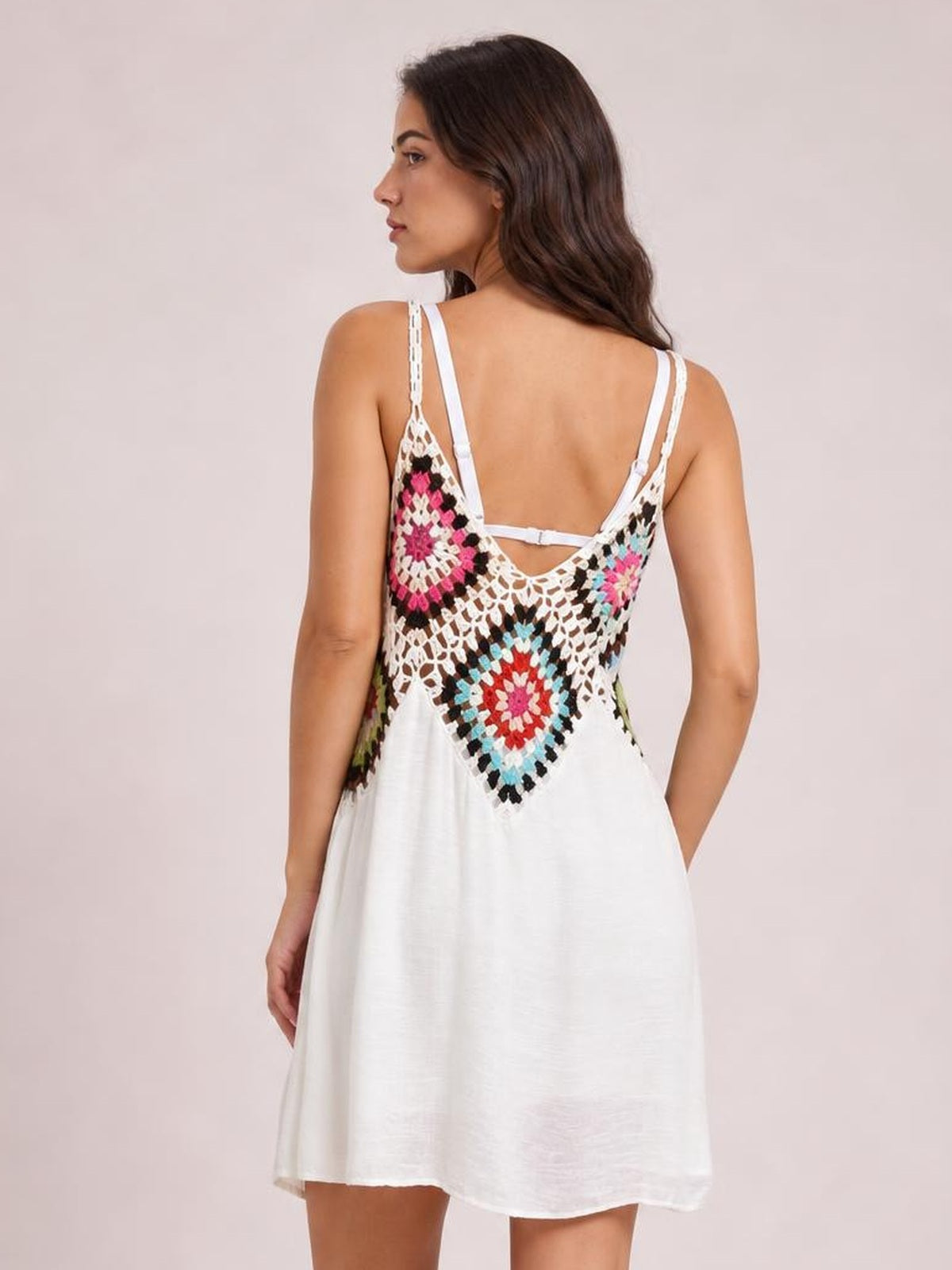 Model shown from behind wearing a white geometric spaghetti-strap cover-up dress with colorful openwork detailing and a loose, flowing mini-length silhouette.