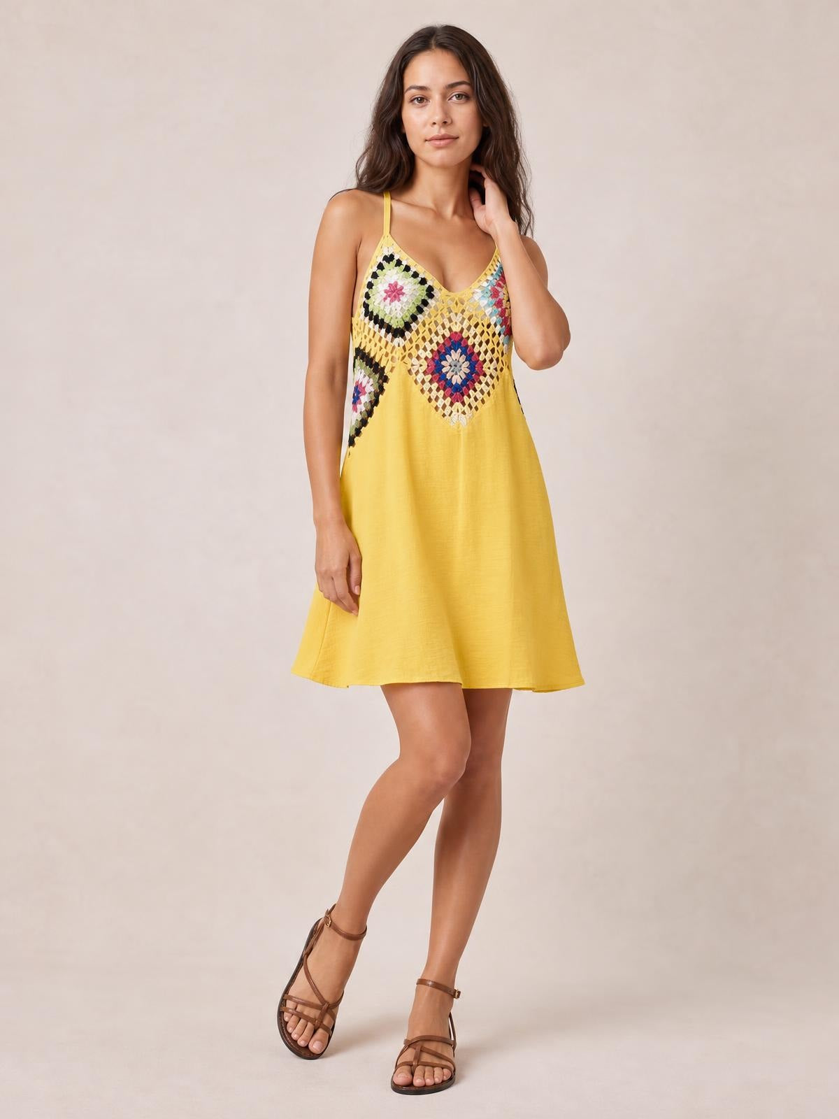 Model poses with one hand in her hair wearing a yellow geometric V-neck spaghetti strap cover up dress with a semi-sheer patterned bodice and relaxed short A-line silhouette.