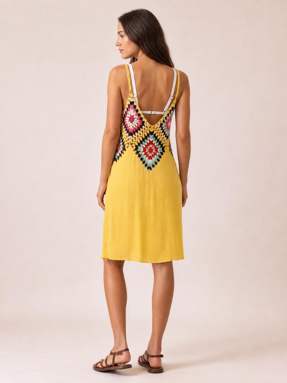 A model stands in profile-back view wearing a yellow spaghetti-strap cover-up dress with a V-back, colorful geometric pattern, and relaxed knee-length silhouette.