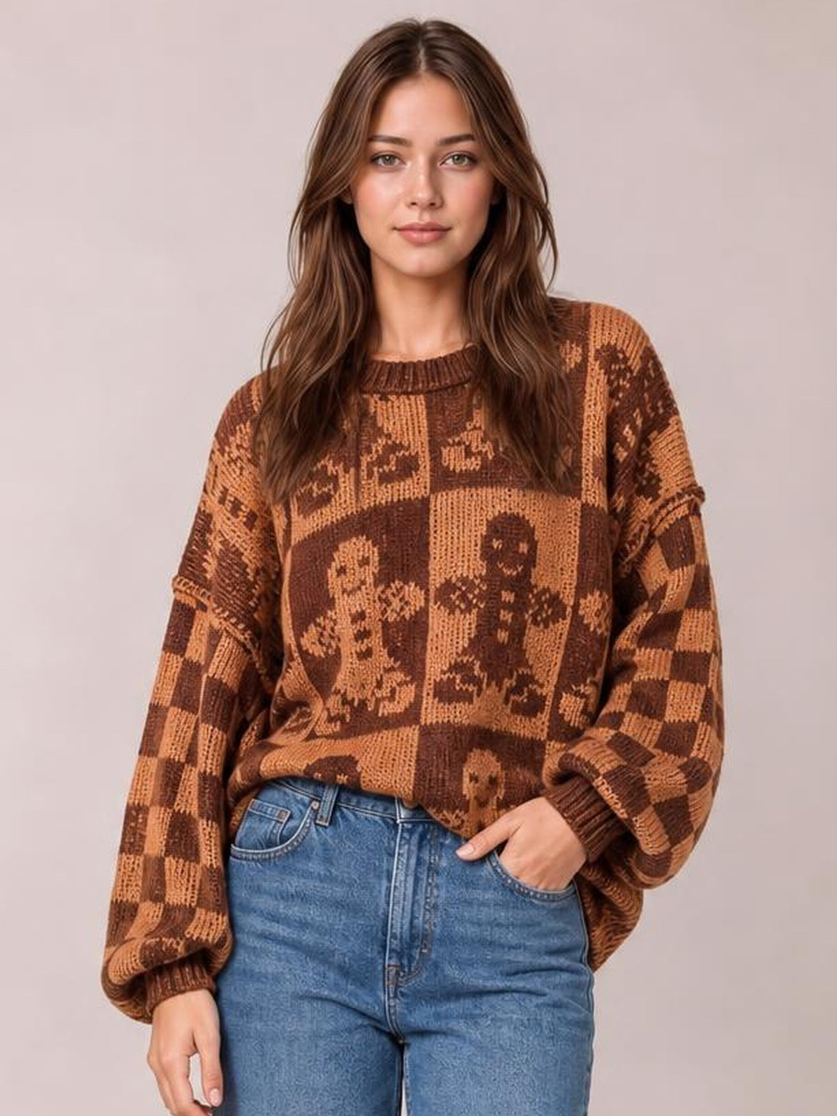 Model poses with one hand in her jeans pocket, wearing a brown and tan gingerbread man sweater with a round neck, drop shoulders, and relaxed silhouette.