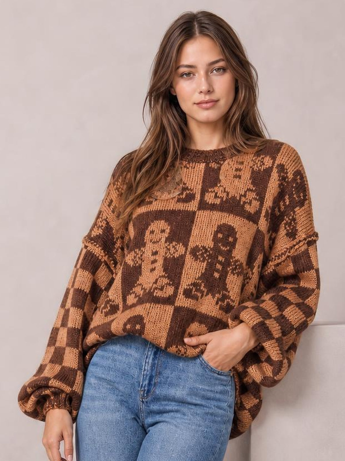 A model poses in a relaxed, loose-fit brown and tan gingerbread man sweater with a round neck, drop shoulders, long sleeves, and ribbed cuffs.