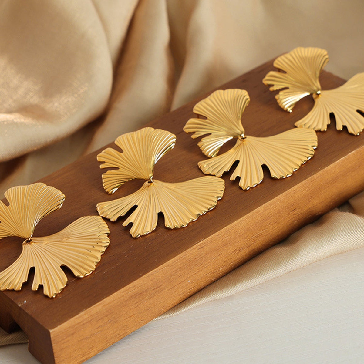 Gold-tone Ginkgo Biloba stud earrings feature elongated fan-shaped leaf silhouettes with fine ribbed detailing and a polished 18K-plated finish.