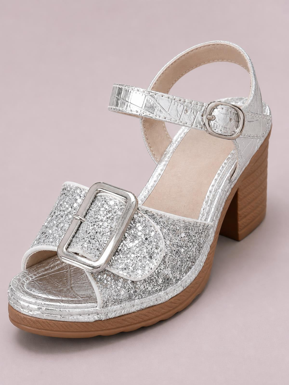 Silver glitter block heel sandals feature open toes, wide buckle straps, an ankle buckle, and a comfortable mid-height wedge-style heel.