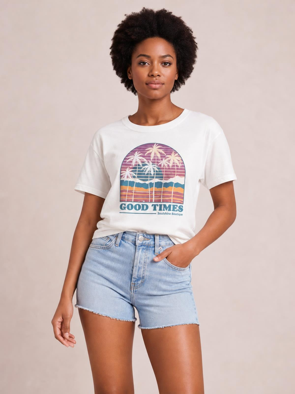 Model wearing a white graphic round neck short sleeve T-shirt with a colorful palm tree print and relaxed silhouette, posing with one hand in her shorts pocket.