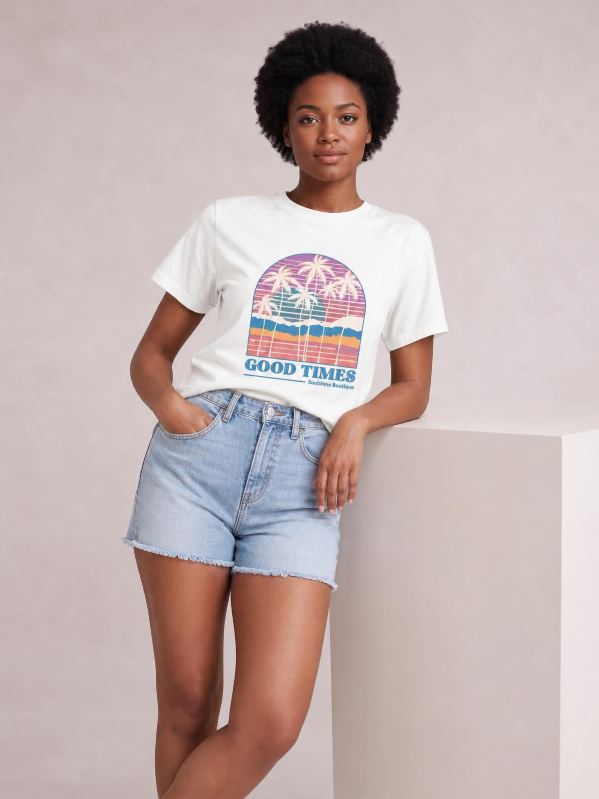 Model poses in a white graphic round neck short sleeve T-shirt with a relaxed silhouette, tucked into high-waisted denim shorts.
